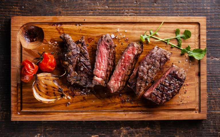 Sliced medium rare grilled Beef steak Ribeye with grilled onions and cherry tomatoes on cutting board on wooden background